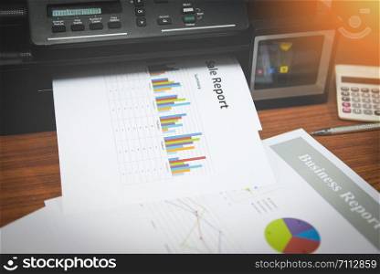 printer printing business reports sale and pile of documents report graph chart on a table at office