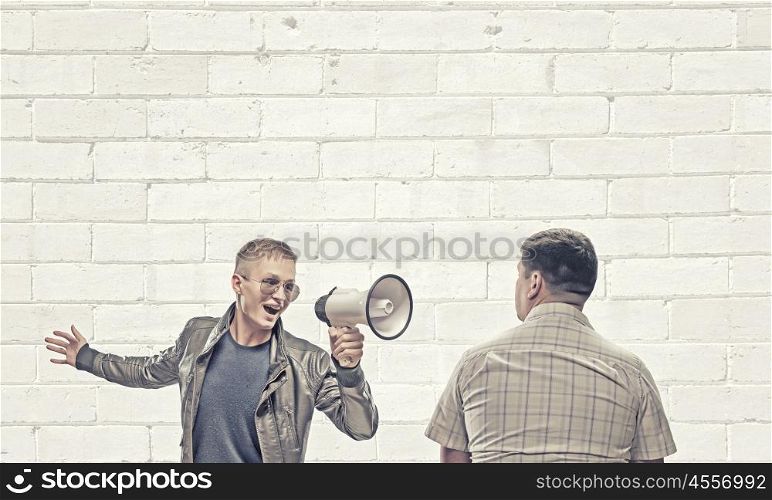 Problem of generation conflict. Young man in casual screaming aggressively in megaphone on adult man