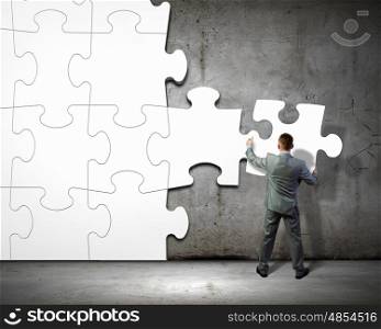 Problem solving. Image of businessman compiling macro white puzzle. Building business