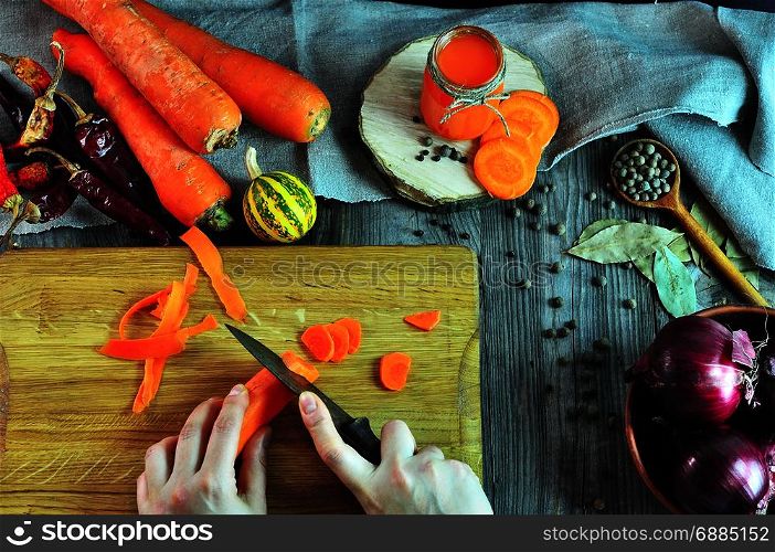 process of cutting a fresh carrot with a knife to make juice, two female hands cutting a vegetable on a kitchen wooden board