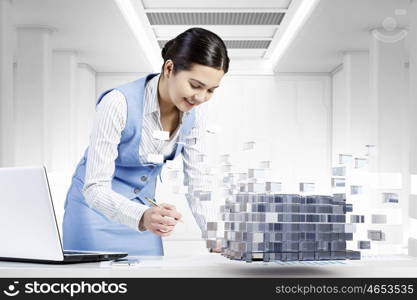 Process of new technologies intergration . Young smiling businesswoman working with laptop and digital levitating cube