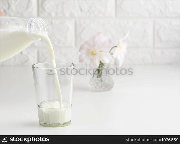 process of pouring fresh milk from a plastic bottle into a glass cup, white table
