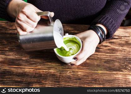 Process of pouring milk in matcha tea cup. Process of pouring milk in matcha tea cup for make latte art. Close up hands