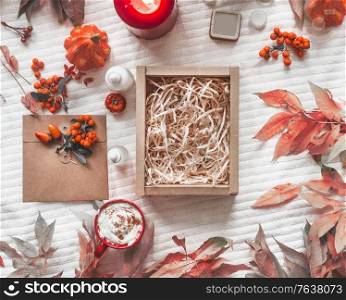 Product eco friendly packaging with empty cardboard boxes and wood chips surrounded by pumpkin, leaves, products, candle and wild berries. Hot chocolate with cream. White blanket background. Top view