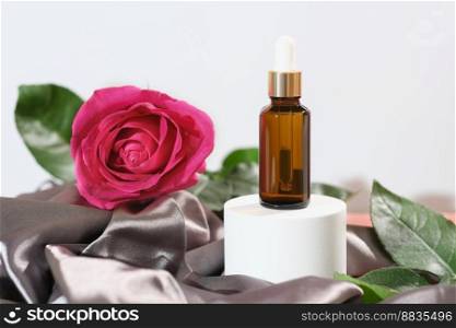 Product for skincare based on rose oil, essential oil solution ina dropper bottle, brown pipette bottle and fresh pink rose flower next to silk textile cloth. Product for skincare based on rose oil, essential oil solution ina dropper bottle, brown pipette bottle and fresh pink rose flower next to silk textile cloth.