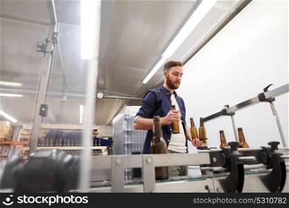 production, business and people concept - men with bottles on conveyor at craft brewery or non-alcoholic beverage plant. men with bottles on conveyor at craft beer brewery
