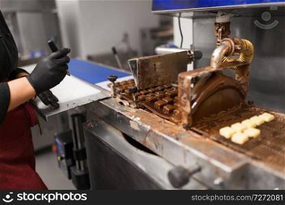 production, candy shop and people concept - confectioner making candies by chocolate coating machine at confectionery. candies making by chocolate coating machine