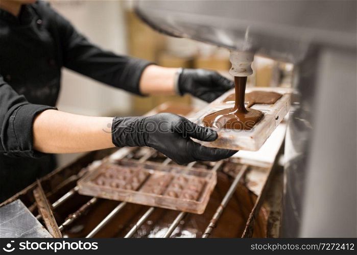 production, cooking and people concept - confectioner filling candy mold with chocolate at confectionery shop. confectioner makes chocolate candies at sweet-shop