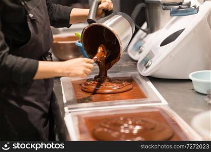 production, cooking and people concept - confectioner filling mold with chocolate at confectionery shop. confectioner makes chocolate dessert at sweet-shop