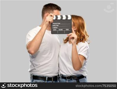 production, filmmaking and entertainment concept - portrait of happy couple in white t-shirts with clapperboard over grey background. happy couple in white t-shirts with clapperboard