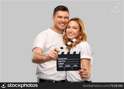 production, filmmaking and entertainment concept - portrait of happy couple in white t-shirts with clapperboard over grey background. happy couple in white t-shirts with clapperboard