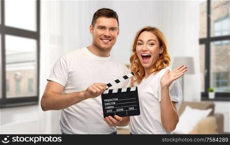 production, filmmaking and entertainment concept - portrait of happy couple in white t-shirts with clapperboard over home background. happy couple in white t-shirts with clapperboard