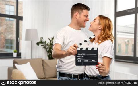 production, filmmaking and entertainment concept - portrait of happy couple in white t-shirts with clapperboard over home background. happy couple in white t-shirts with clapperboard