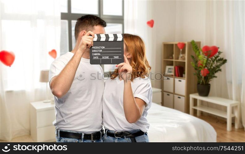 production, filmmaking and valentine&rsquo;s day concept - portrait of happy couple in white t-shirts with clapperboard over home bedroom decorated with heart shaped balloons background. happy couple in white t-shirts with clapperboard