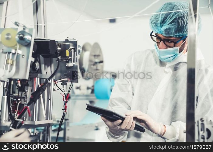 Production line worker with face mask working in electronic factory . Concept of protective action and quarantine to stop spreading of Coronavirus Disease 2019 or COVID-19 .