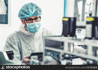 Production line worker with face mask working in electronic factory . Concept of protective action and quarantine to stop spreading of Coronavirus Disease 2019 or COVID-19 .