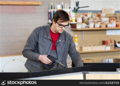 production, manufacture and industry concept - assembler working with electric screwdriver making furniture at workshop. assembler with screwdriver making furniture