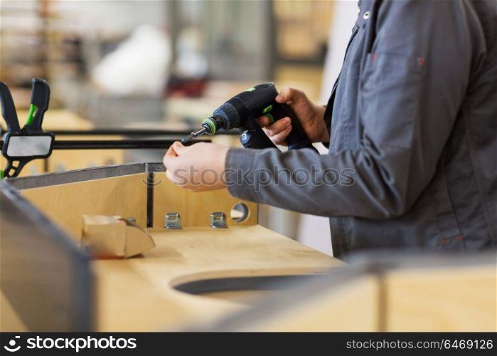 production, manufacture and industry concept - assembler working with electric screwdriver making furniture at workshop. assembler with screwdriver making furniture