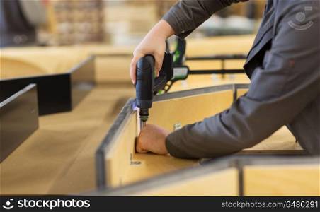 production, manufacture and industry concept - assembler working with electric screwdriver making furniture at workshop. assembler with screwdriver making furniture. assembler with screwdriver making furniture