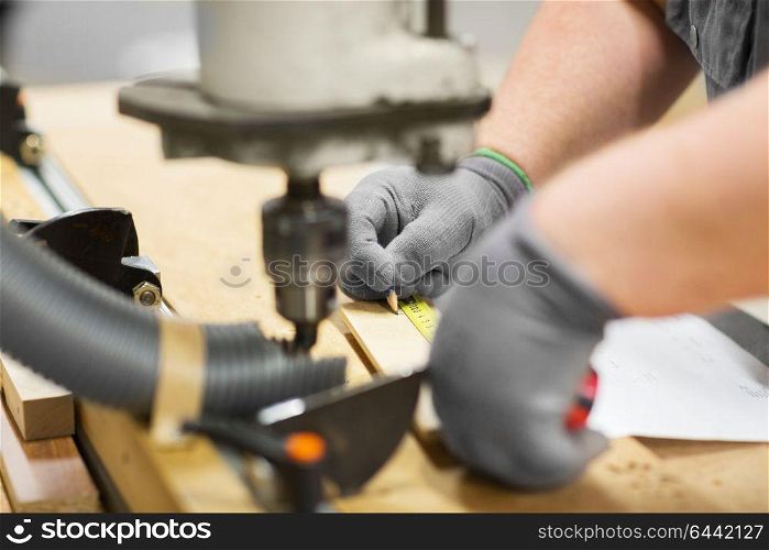 production, manufacture and woodworking industry concept - carpenter hands with pencil measuring board by ruler at workshop on workbench of drill press machine. carpenter with ruler measuring board at workshop