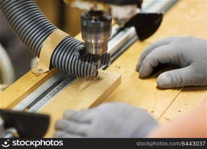 production, manufacture and woodworking industry concept - hands of carpenter working with drill press and board at workshop. carpenter with drill press and board at workshop