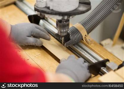 production, manufacture and woodworking industry concept - hands of carpenter working with drill press and board at workshop. carpenter with drill press and board at workshop