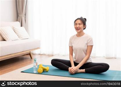 Productive activity concept a girl with a bun sitting on the rectangular green mat stretching her both legs parallel to the floor.