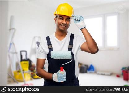 profession, building and repair concept - happy smiling indian builder or painter in helmet with paint roller over empty room with construction equipment background. happy indian painter or builder with paint roller