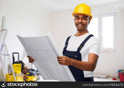 profession, building and repair concept - happy smiling indian builder or repairman in helmet with blueprint over empty room with construction equipment background. happy indian builder in helmet with blueprint