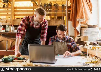 profession, carpentry, technology and people concept - two carpenters with laptop computer and blueprint at workshop