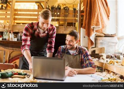 profession, carpentry, technology and people concept - two carpenters with laptop computer and blueprint at workshop