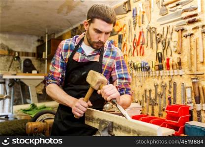 profession, carpentry, woodwork and people concept - carpenter with hammer and chisel processing wood plank at workshop
