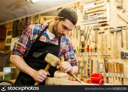 profession, carpentry, woodwork and people concept - carpenter with hammer and chisel processing wood plank at workshop