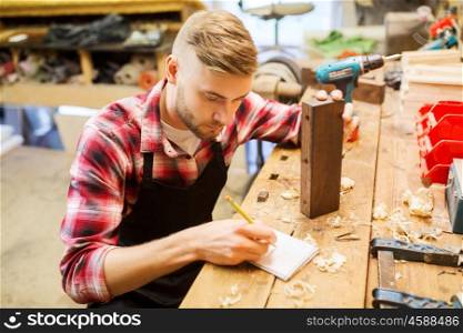 profession, carpentry, woodwork and people concept - carpenter with wood plank and notebook working at workshop