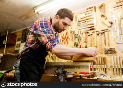 profession, carpentry, woodwork and people concept - carpenter working with plane and wood plank at workshop