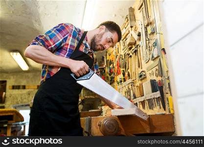 profession, carpentry, woodwork and people concept - carpenter working with saw and wood plank at workshop