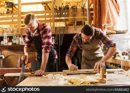 profession, carpentry, woodwork and people concept - carpenters working with saw and wood plank at workshop
