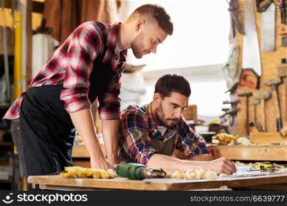 profession, carpentry, woodwork and people concept - two carpenters with blueprint working at workshop. carpenters with blueprint working at workshop