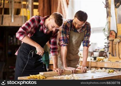 profession, carpentry, woodwork and people concept - two carpenters with electric drill drilling wooden board at workshop. carpenters with drill drilling board at workshop