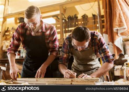 profession, carpentry, woodwork and people concept - two carpenters with ruler measuring wood plank at workshop