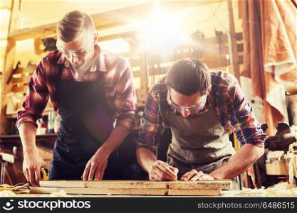 profession, carpentry, woodwork and people concept - two carpenters with ruler measuring wood plank at workshop. carpenters with ruler and wood plank at workshop. carpenters with ruler and wood plank at workshop
