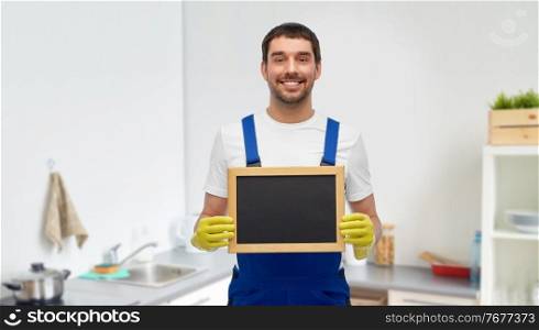 profession, cleaning service and plumbing concept - happy smiling male worker, plumber or cleaner showing chalkboard over home room background. male cleaner with chalkboard at at kitchen