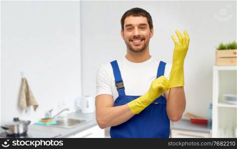 profession, cleaning service and plumbing concept - happy smiling male worker, plumber or cleaner in overall wearing gloves over home room background. happy male worker or cleaner in gloves at kitchen