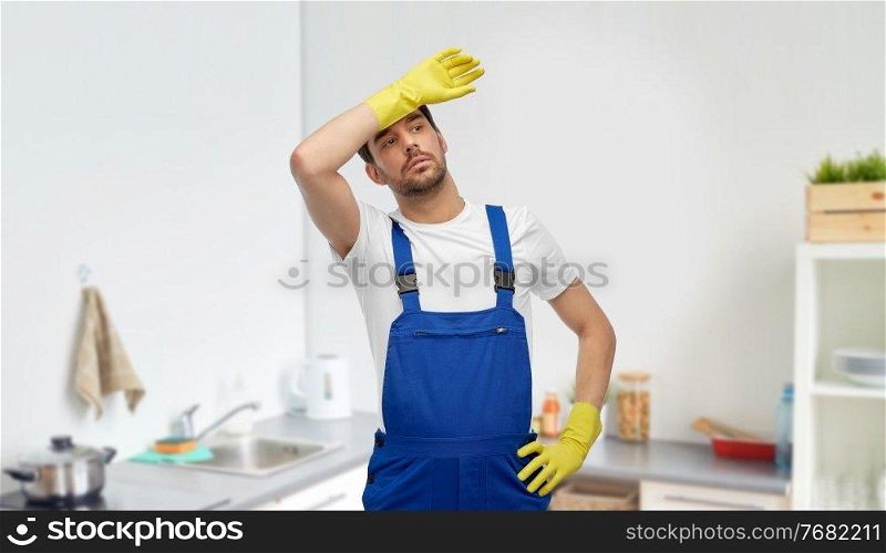 profession, cleaning service and plumbing concept - happy smiling male worker, plumber or cleaner r in overall and gloves over home room background. tired male worker or cleaner in gloves at kitchen