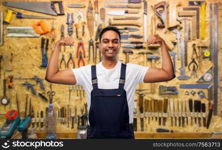profession, construction and building concept - happy smiling indian worker or builder showing his power over work tools on background. smiling indian worker or builder showing his power