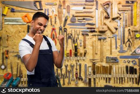 profession, construction and building concept- happy smiling indian worker or builder celebrating success over work tools on background. happy indian worker or builder celebrating success