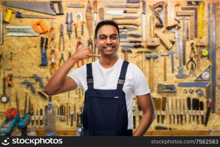 profession, construction and building concept- happy smiling indian worker or builder making phone call gesture over work tools on background. happy worker or builder making phone call gesture