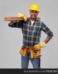 profession, construction and building - happy smiling indian carpenter or builder in helmet with tool belt and wooden boards over grey background. happy indian worker or builder with wooden boards