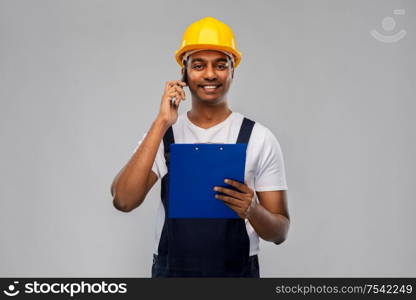 profession, construction and building - happy smiling indian worker or builder in helmet with clipboard calling on smartphone over grey background. indian builder with clipboard calling on cellphone