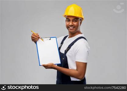 profession, construction and building - happy smiling indian worker or builder in helmet with clipboard and pencil over grey background. happy builder in helmet with clipboard and pencil